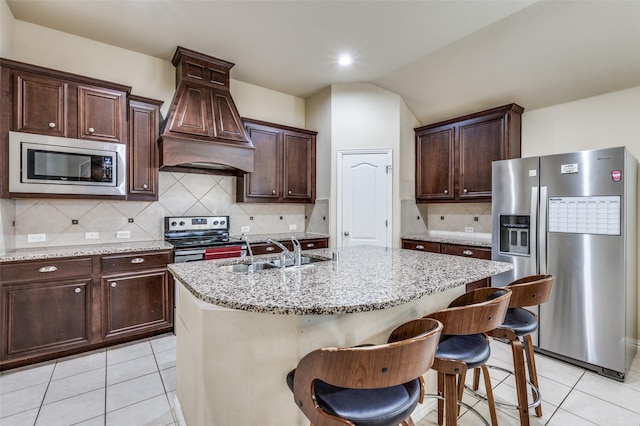 kitchen featuring light stone counters, a center island with sink, light tile patterned flooring, a sink, and appliances with stainless steel finishes