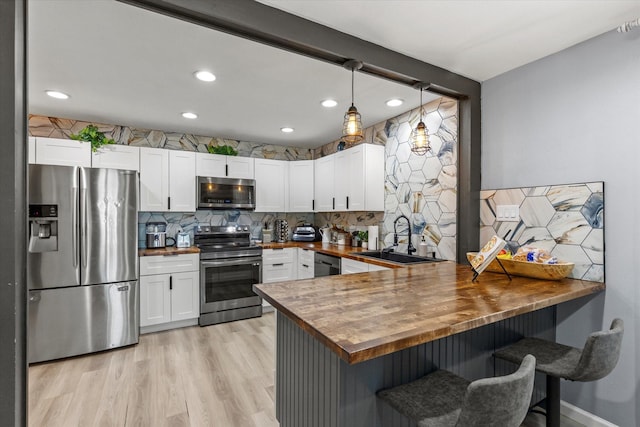 kitchen with a peninsula, a sink, butcher block countertops, stainless steel appliances, and tasteful backsplash