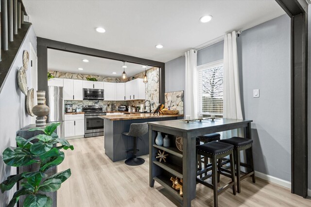 kitchen with butcher block countertops, a sink, stainless steel appliances, a peninsula, and white cabinets