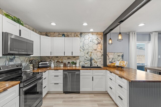 kitchen featuring wood counters, backsplash, appliances with stainless steel finishes, a peninsula, and white cabinets