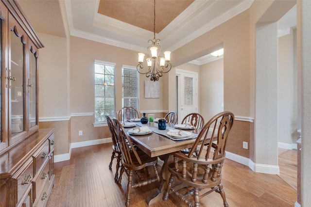 dining space featuring a chandelier, ornamental molding, wainscoting, light wood-type flooring, and a tray ceiling