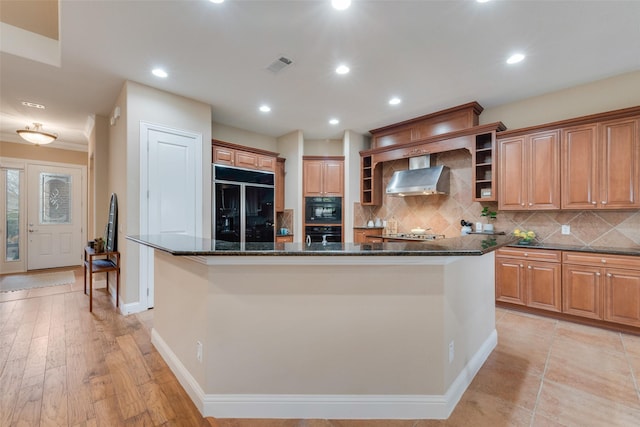 kitchen with high end black fridge, visible vents, wall chimney exhaust hood, a center island, and open shelves