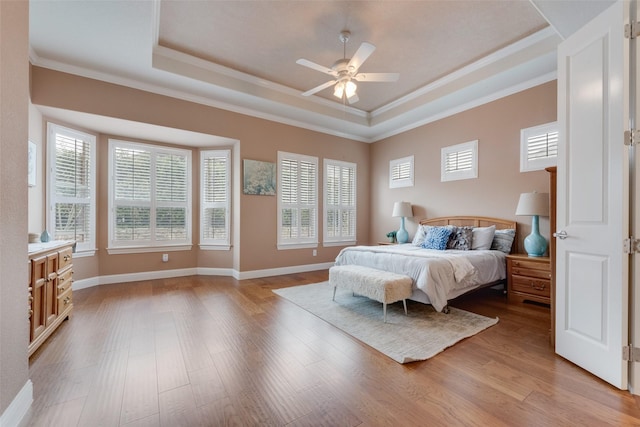 bedroom featuring ceiling fan, baseboards, light wood-style floors, ornamental molding, and a raised ceiling