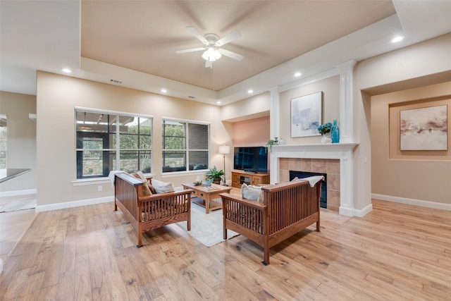 living room featuring a raised ceiling, light wood finished floors, a tile fireplace, and baseboards