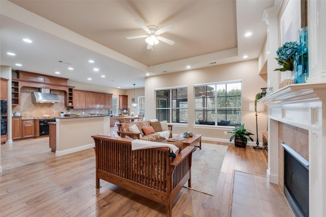 living area with light wood finished floors, baseboards, a tiled fireplace, a tray ceiling, and recessed lighting