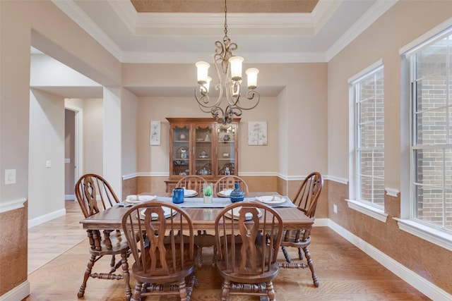 dining area with light wood-style floors, a raised ceiling, a notable chandelier, and ornamental molding