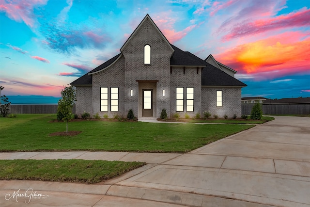 view of front facade featuring brick siding, fence, concrete driveway, roof with shingles, and a front lawn