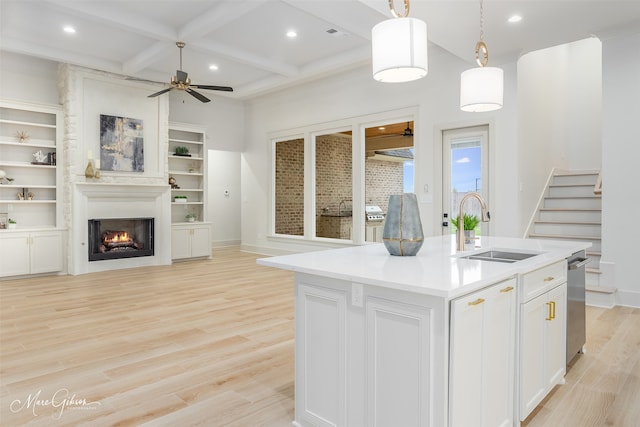 kitchen featuring light wood finished floors, a sink, ceiling fan, a warm lit fireplace, and coffered ceiling