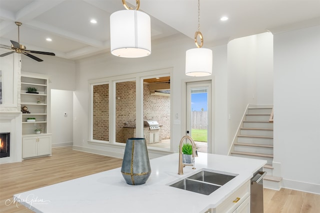 kitchen with a warm lit fireplace, recessed lighting, a sink, beam ceiling, and light wood finished floors