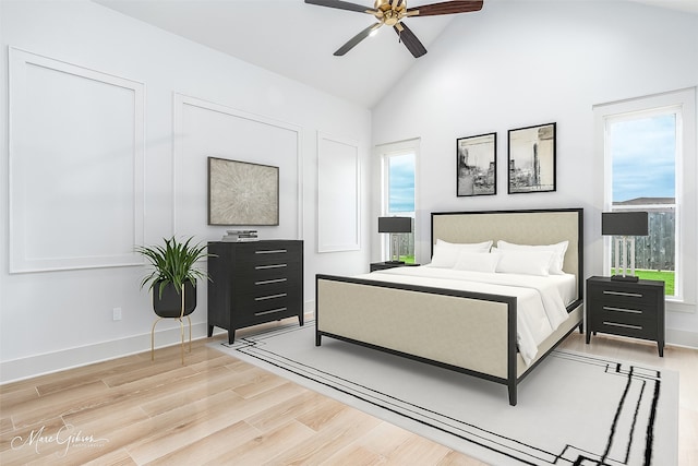 bedroom with high vaulted ceiling, multiple windows, light wood-style flooring, and baseboards