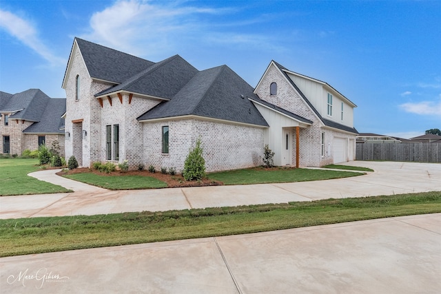 french country style house featuring brick siding, a shingled roof, an attached garage, a front yard, and driveway