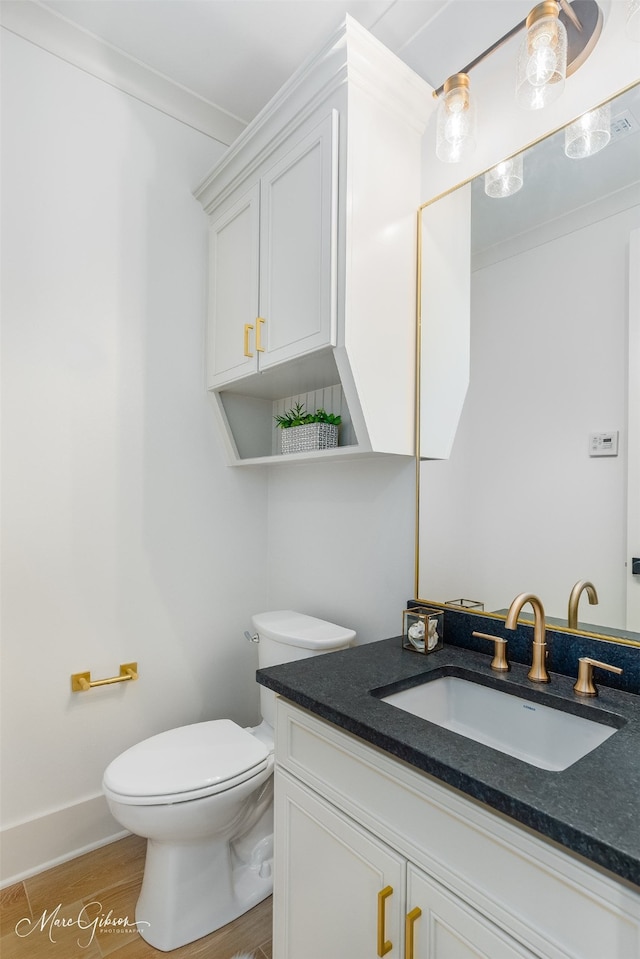 bathroom with toilet, wood finished floors, vanity, baseboards, and crown molding