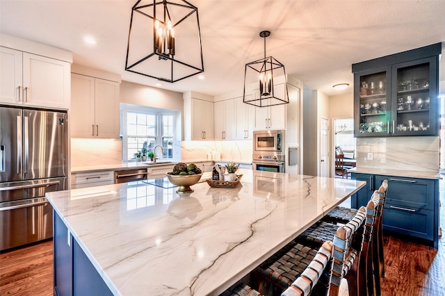 kitchen with a sink, light stone counters, tasteful backsplash, dark wood-style floors, and appliances with stainless steel finishes