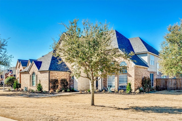 view of front of house featuring brick siding, roof with shingles, and fence