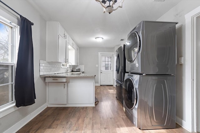 laundry area with stacked washer and dryer, hardwood / wood-style floors, laundry area, and baseboards