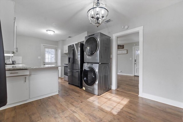 clothes washing area with baseboards, visible vents, stacked washer / drying machine, an inviting chandelier, and light wood-style floors