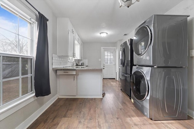 laundry room with laundry area, baseboards, stacked washing maching and dryer, and hardwood / wood-style flooring