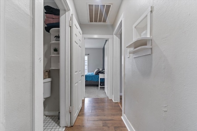 hall with baseboards, visible vents, wood finished floors, and a textured wall