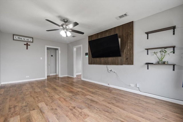 unfurnished living room featuring a ceiling fan, baseboards, visible vents, and wood finished floors