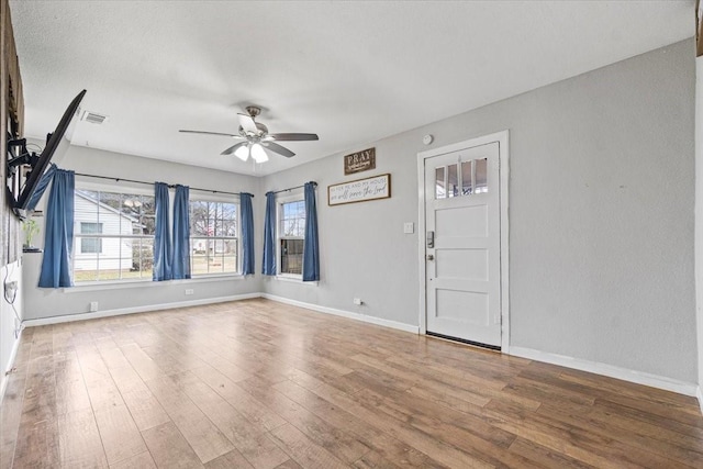 empty room with a ceiling fan, baseboards, visible vents, and wood finished floors