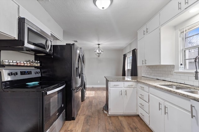 kitchen featuring light wood-style flooring, range with electric stovetop, a sink, white cabinetry, and stainless steel microwave