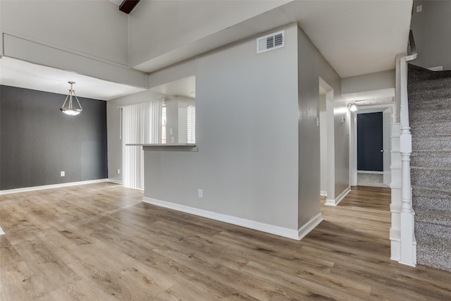 empty room with stairway, wood finished floors, visible vents, and baseboards