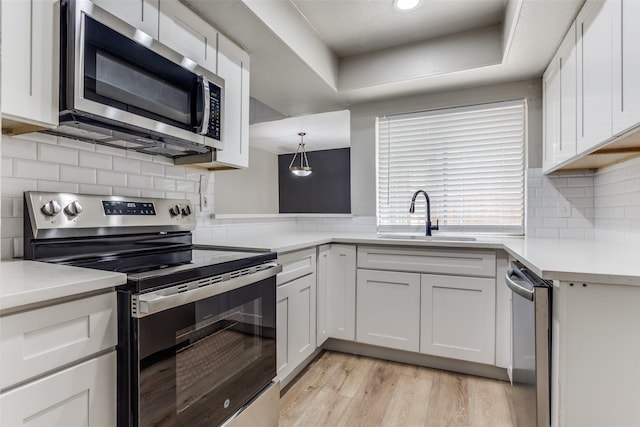 kitchen featuring light countertops, appliances with stainless steel finishes, white cabinetry, a sink, and light wood-type flooring