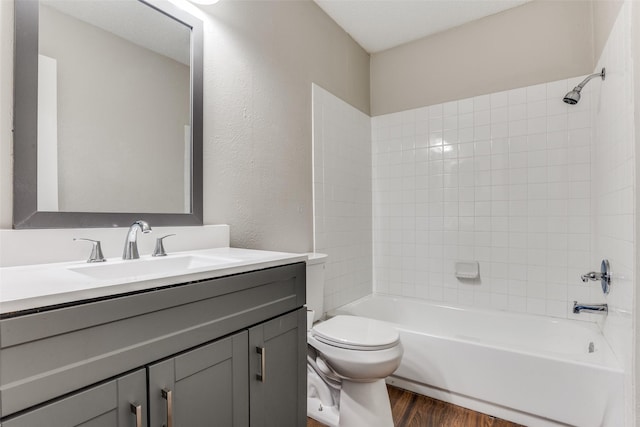 bathroom with a textured wall, toilet, shower / tub combination, wood finished floors, and vanity