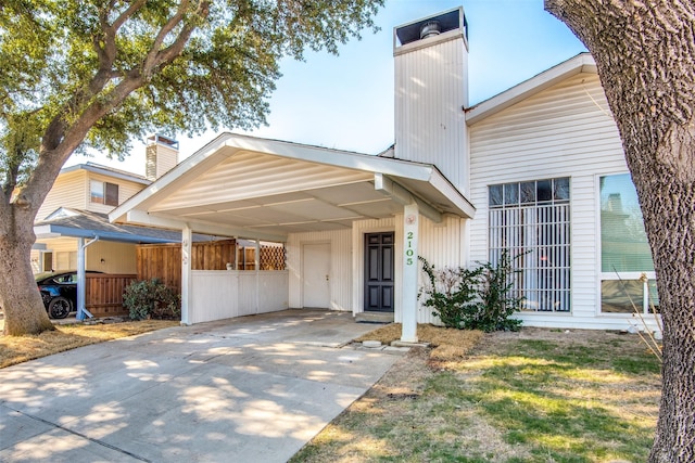 view of front of property featuring an attached carport, driveway, a chimney, and fence