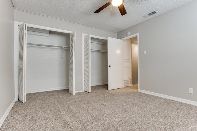 unfurnished bedroom featuring a textured ceiling, carpet flooring, visible vents, and multiple closets