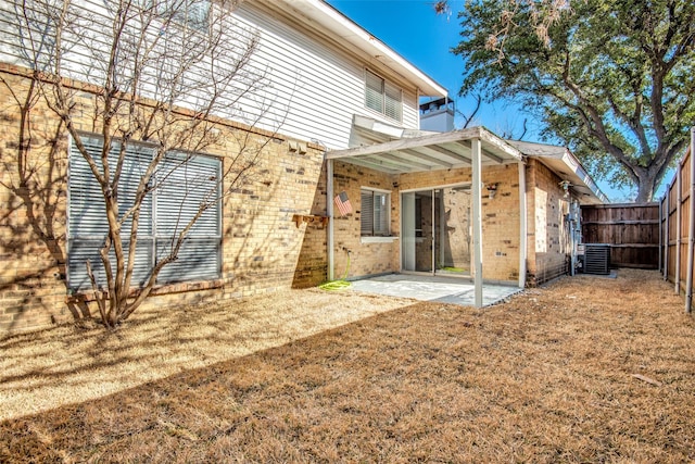 rear view of property with a patio, a fenced backyard, central AC, brick siding, and a yard