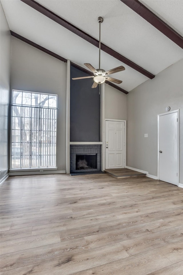 unfurnished living room with ceiling fan, baseboards, a brick fireplace, beam ceiling, and light wood finished floors