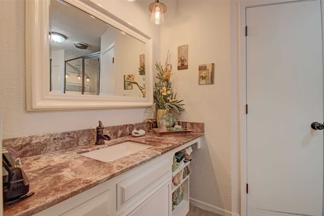 bathroom featuring a shower with shower door, baseboards, a textured ceiling, and vanity