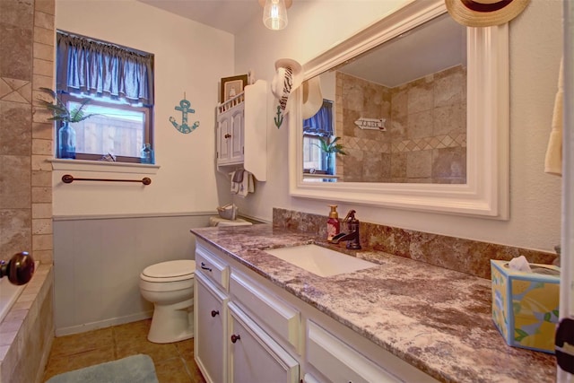 bathroom featuring vanity, a wainscoted wall, tiled shower, tile patterned floors, and toilet