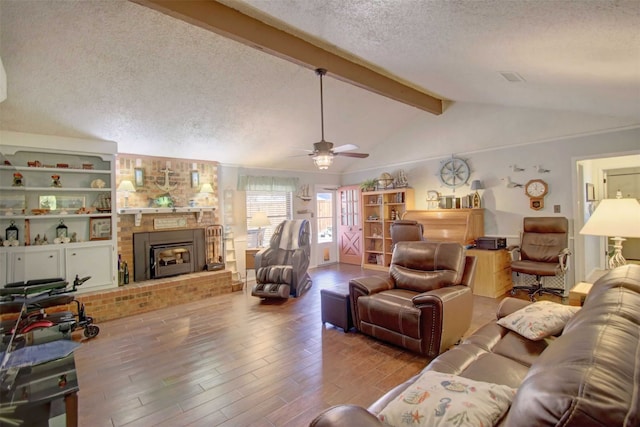 living area featuring a ceiling fan, wood finished floors, lofted ceiling with beams, a textured ceiling, and a brick fireplace