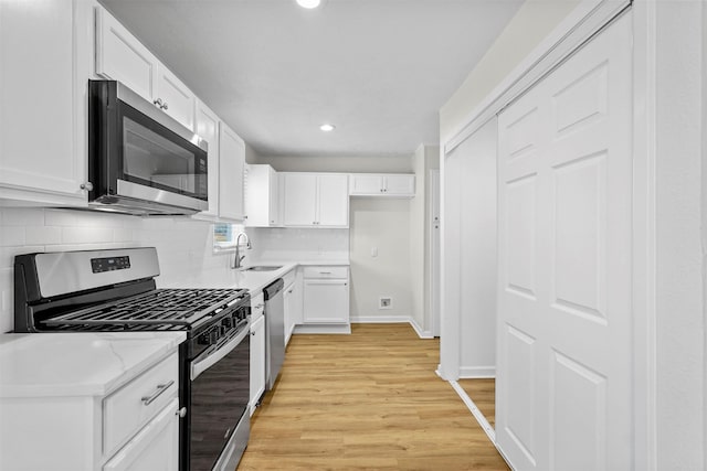 kitchen featuring decorative backsplash, appliances with stainless steel finishes, light wood-style floors, white cabinets, and a sink