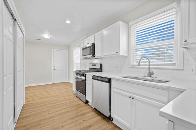 kitchen featuring light wood finished floors, appliances with stainless steel finishes, light countertops, white cabinetry, and a sink