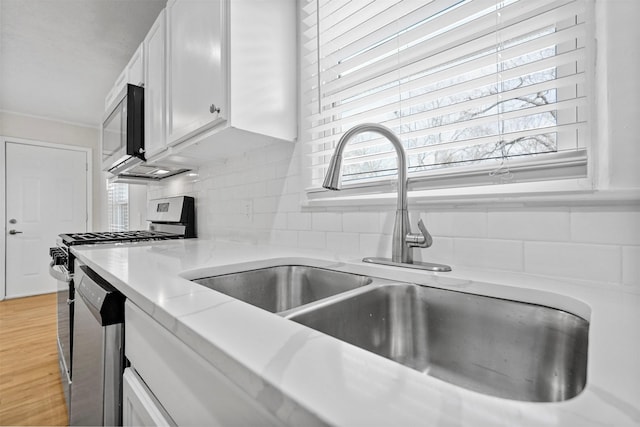 kitchen with decorative backsplash, white cabinets, appliances with stainless steel finishes, light wood-style floors, and a sink