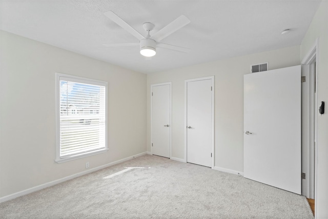 unfurnished bedroom featuring baseboards, visible vents, ceiling fan, and light colored carpet