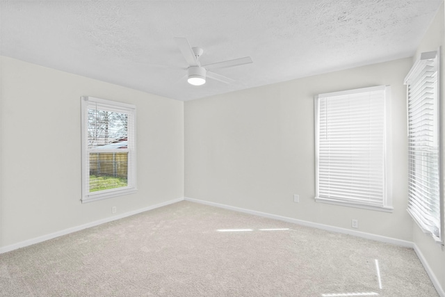 spare room featuring light colored carpet, ceiling fan, a textured ceiling, and baseboards