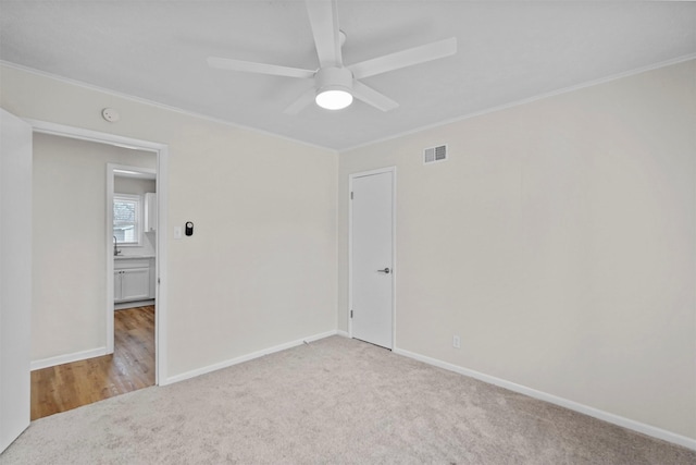 spare room featuring light carpet, visible vents, a ceiling fan, and ornamental molding