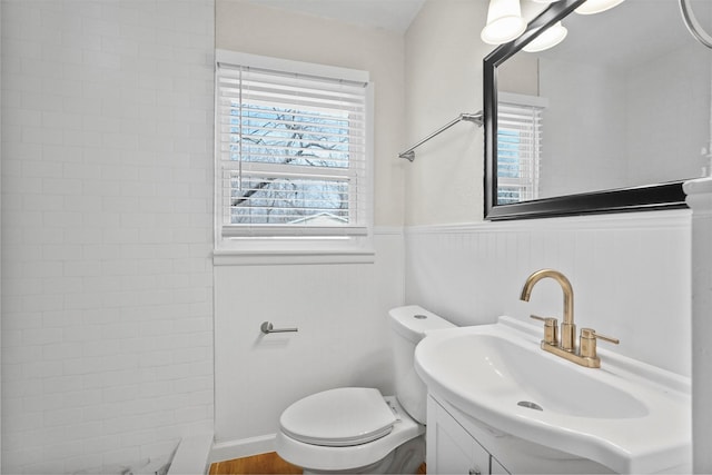 full bathroom with wainscoting, vanity, toilet, and tiled shower