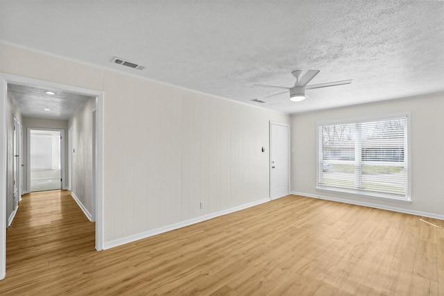 spare room featuring light wood finished floors, visible vents, baseboards, a ceiling fan, and a textured ceiling