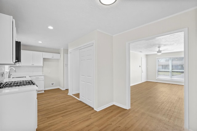 kitchen with light wood-type flooring, a sink, white cabinetry, and baseboards