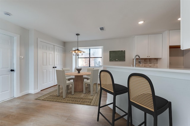 kitchen with visible vents, a breakfast bar area, decorative light fixtures, white cabinetry, and a sink