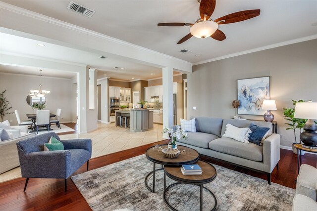 living area with light wood finished floors, visible vents, ceiling fan with notable chandelier, and baseboards