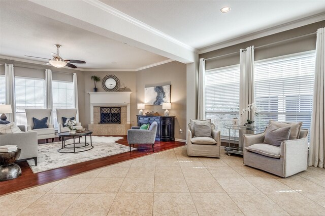 living area with tile patterned floors, a ceiling fan, a fireplace, crown molding, and baseboards