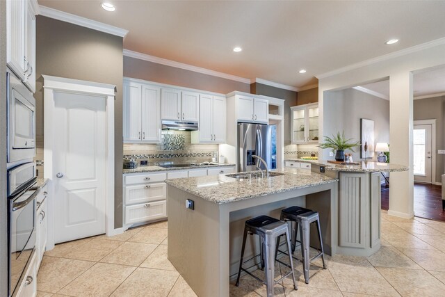 kitchen featuring a breakfast bar, a sink, under cabinet range hood, backsplash, and stainless steel appliances