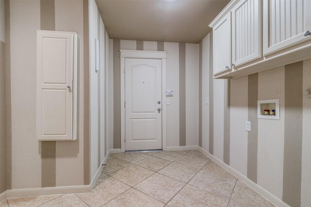 clothes washing area featuring light tile patterned flooring, cabinet space, baseboards, and washer hookup