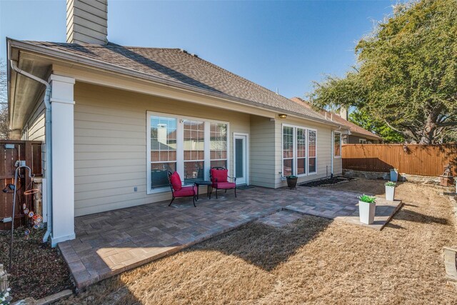 back of house featuring a patio area, a chimney, roof with shingles, and fence